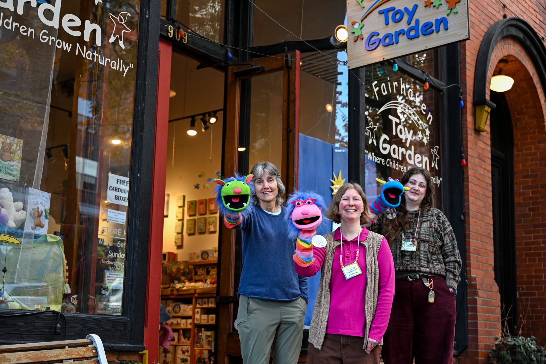 Owner and staff of Fairhaven Toy Garden pose with puppets outside the storefront.