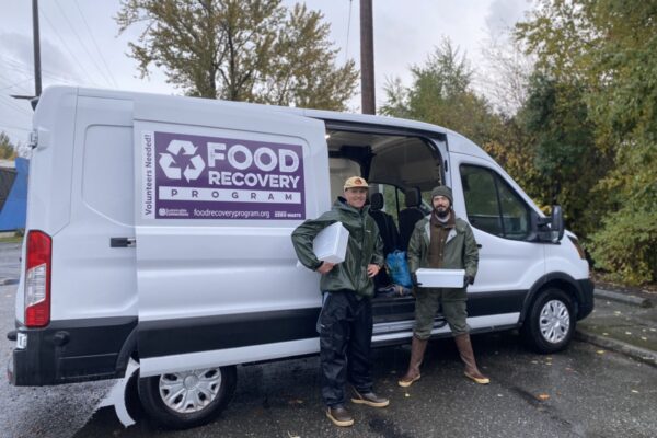 two people with food recovery tubs standing in front of the food recovery van