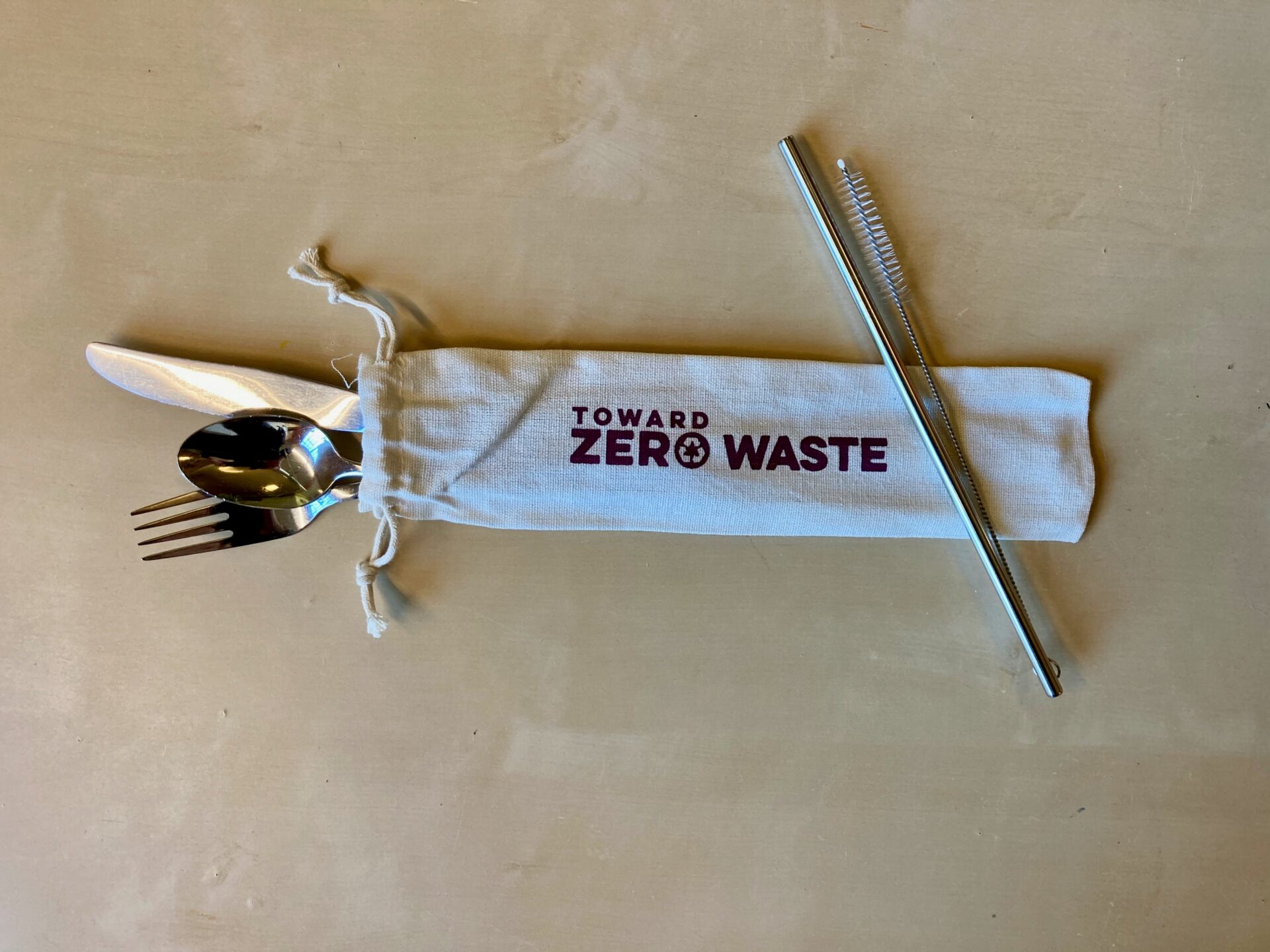 Burlap bag with silverware and a reusable straw with the Toward Zero Waste logo