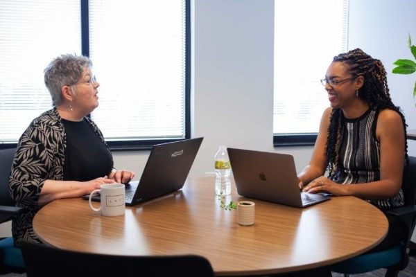 Women speaking at a table with laptops