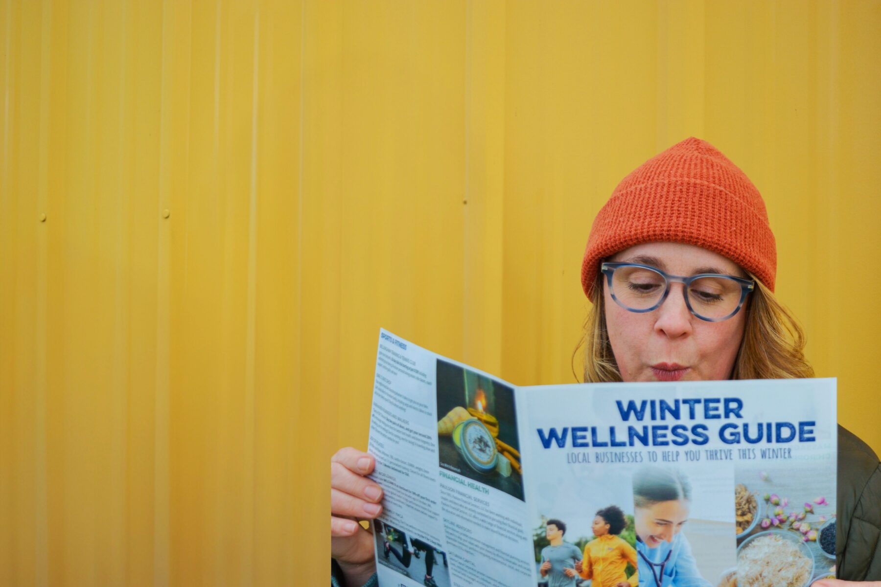 SC Homepage_Winter Wellness 2026 Photo of person with red hat looking at a printed Winter Wellness guide looking interested in front of a yellow background.