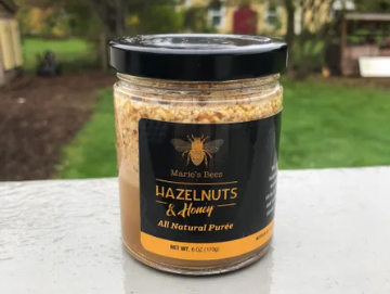 A jar of Hazelnut & Honey Puree from Marie's Bees sits on a table in a backyard.